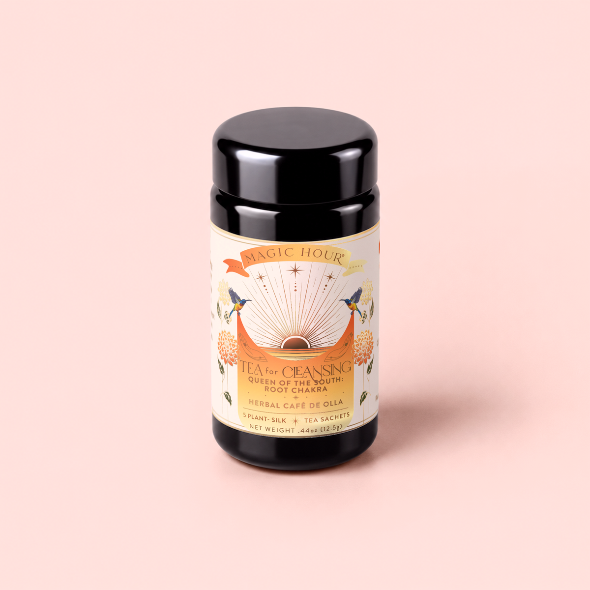 A black canister labeled “Tea for Cleansing: Queen of the South: Herbal Cafe de Olla” rests on a pale pink background. The label displays floral designs, two hummingbirds, and celestial motifs, with text highlighting its antioxidant-rich and caffeine-free herbal cafe de olla tea sachets.