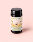 A black canister labeled “Tea for Beauty: Renewal: Peach, Goji & Rose Oolong Tea” sits on a soft pink background, its label adorned with gold accents and decorated with floral and sun illustrations.