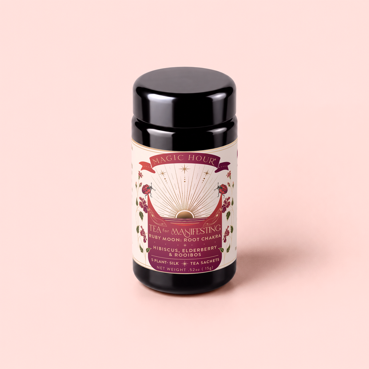 A black tea canister labeled “Tea for Manifesting: Ruby Moon” rests on a light pink background. The label features floral illustrations and a celestial design with rays, and the text describes a vitamin C rich herbal blend of hibiscus, elderberry, and passionfruit.