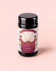 A black tea canister labeled “Tea for Manifesting: Ruby Moon” rests on a light pink background. The label features floral illustrations and a celestial design with rays, and the text describes a vitamin C rich herbal blend of hibiscus, elderberry, and passionfruit.