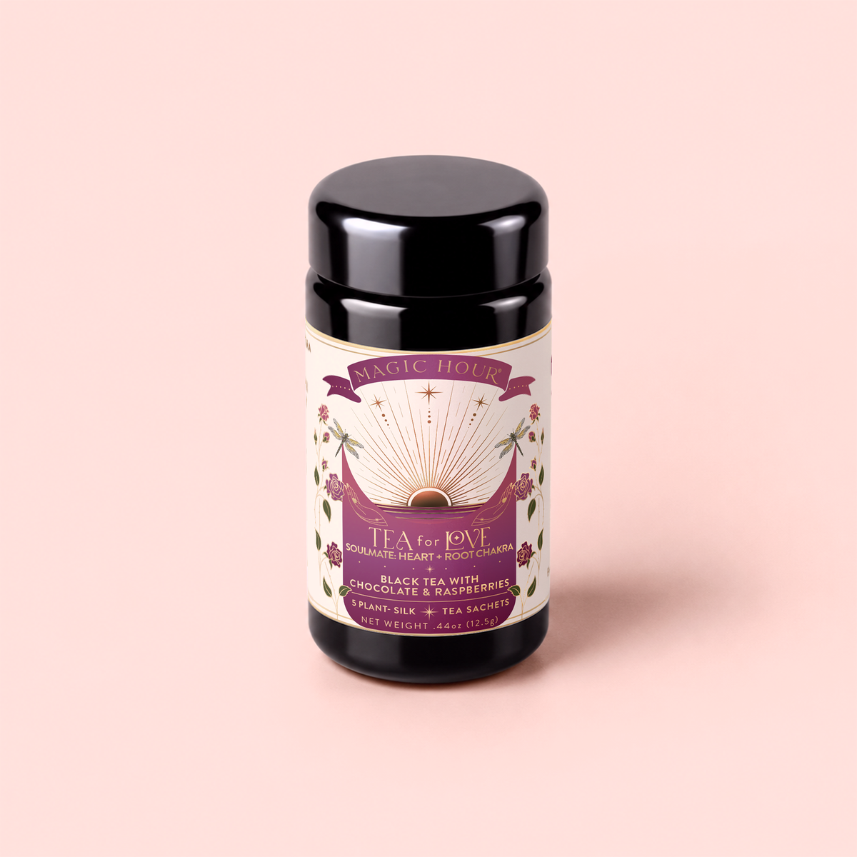 A black tea canister labeled “Tea for Love: Soulmate: Black Tea with Chocolate & Raspberries” sits on a light pink background. The label features an open book, flowers, and hearts in purple, gold, and white. This enchanting Fair Trade blend combines black tea with chocolate and raspberries to capture romance in every cup.