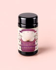 A black tea canister labeled “Tea for Love: Soulmate: Black Tea with Chocolate & Raspberries” sits on a light pink background. The label features an open book, flowers, and hearts in purple, gold, and white. This enchanting Fair Trade blend combines black tea with chocolate and raspberries to capture romance in every cup.