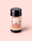 A black tea canister labeled “Tea for Rest: Venus: Mango Blossom & Nervines Herbal Tea” features a vibrant label adorned with flowers, stars, and sun rays, set against a soft pink background. This soothing herbal blend is specially crafted to encourage relaxation while supporting skin hydration and collagen production.