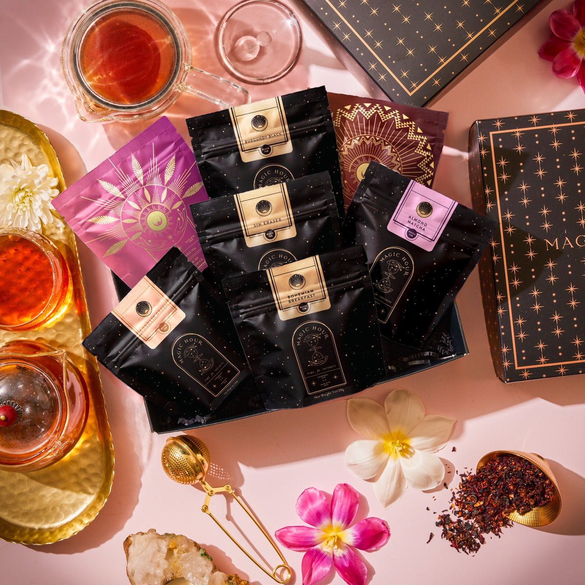 The Best of Magic Hour Sampler Set with Tea in Hand Teapot, featuring five organic wellness teas, a glass teapot, loose tea, a tea infuser, and fresh flowers.