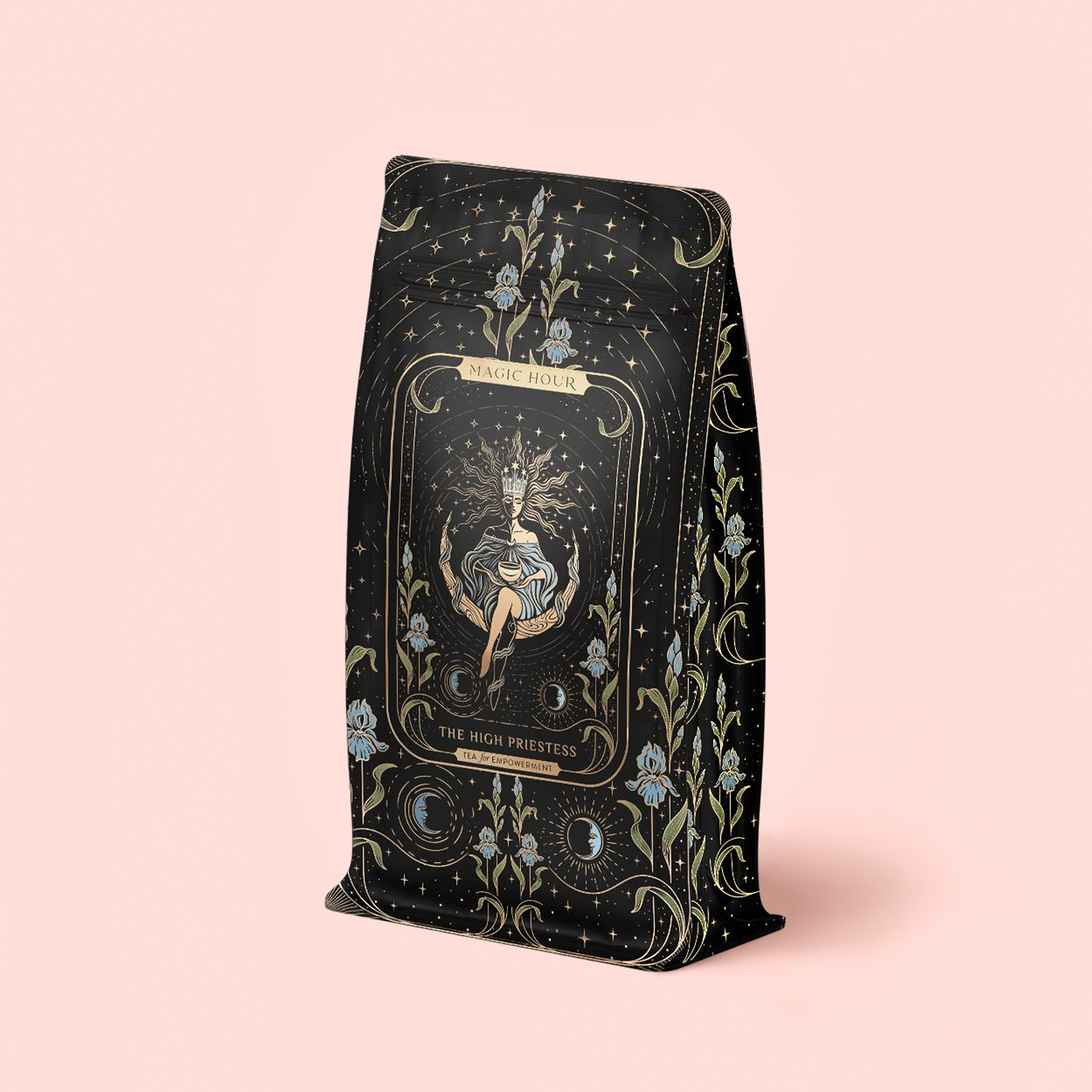 A black and gold refill pouch for The High Priestess Ginger-Mint-Cardamom Tea displays celestial and floral motifs; "Magic Hour" and "The High Priestess" appear above an illustrated mystical figure on the front. The soft pink background evokes the enchanting qualities of this organic, caffeine-free tea.