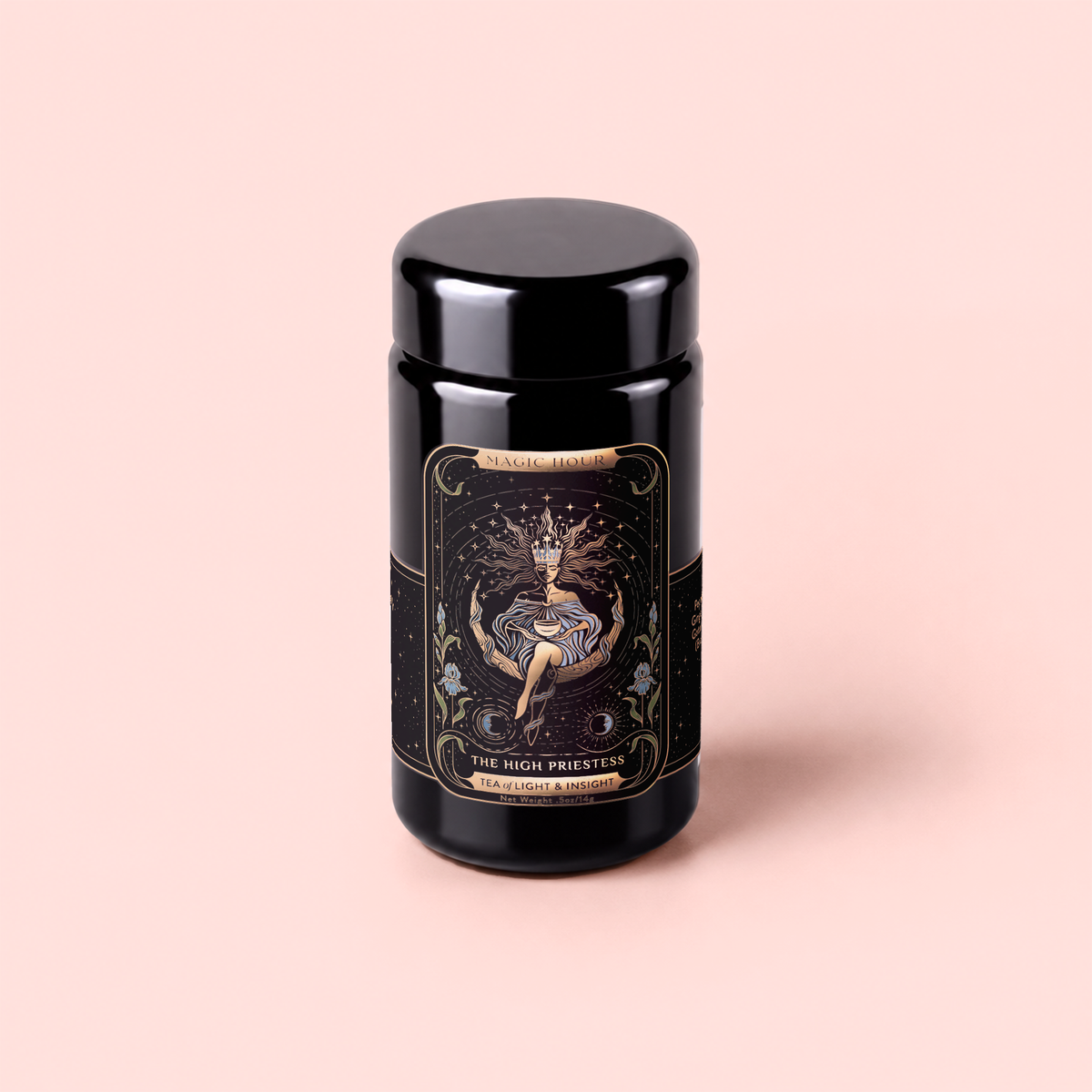 A black tea canister titled “The High Priestess Ginger-Mint-Cardamom Tea Powerful Dreams &amp; Illuminated Insights” sits on a light pink background, its ornate label adorned with a mystical woman, star motifs, and gold detailing—evoking the enchanting allure of dream tea.