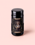 A black tea canister titled “The High Priestess Ginger-Mint-Cardamom Tea Powerful Dreams & Illuminated Insights” sits on a light pink background, its ornate label adorned with a mystical woman, star motifs, and gold detailing—evoking the enchanting allure of dream tea.