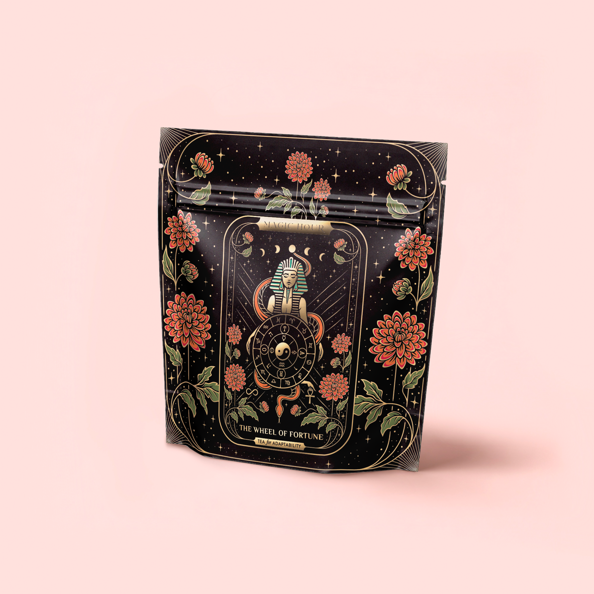 A black resealable pouch with ornate red flowers and gold accents displays a tarot-inspired Wheel of Fortune and Egyptian sphinx, holding The Wheel of Fortune: Ginseng Spice Tea for Adapting to Change, set against a light pink background.
