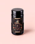 A black jar with a decorative label featuring mystical symbols, floral designs, and text reading “The Wheel of Fortune: Ginseng Spice Tea for Adapting to Change” sits on a light pink background, highlighting its adaptogenic blend ideal for wellness detox rituals.