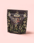 The World: Tea of Infinite Possibiliteas is a decorative pouch featuring a tarot card design with a woman, swirling ribbons, blue lotus, Yunnan black tea motifs, stars, and florals on a soft pink background.