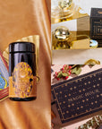 A luxurious tea set includes a black tea tin adorned with intricate gold designs, tarot cards, a tea infuser, and a "Magic Hour" box. Drawing inspiration from the Gem-Inspired Tea Ritual, this arrangement is elegantly displayed on shimmering golden fabric, evoking an enchanting and mystical atmosphere similar to the Topaz November Birthstone Mini Gift Set.