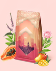 A decorative pink and gold package of "Turkish Delight" tea features a cityscape design, surrounded by illustrated papaya, mango, rose, and other flowers against a light pink background. Inspired by Istanbul, this caffeine-free herbal blend captures the enchanting spirit of Turkish delight in every sip.