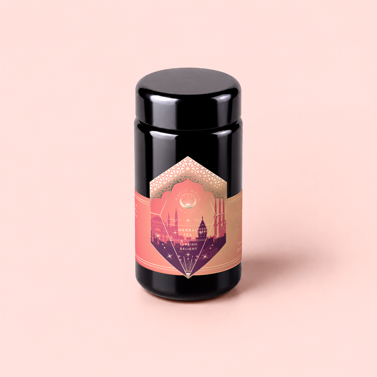 A black cylindrical jar with a pink and gold label adorned with geometric patterns and building silhouettes, set against a light pink background. Turkish Delight is a caffeine-free herbal tea inspired by the classic flavors of Turkish delight, bringing a taste of tradition to your cup.