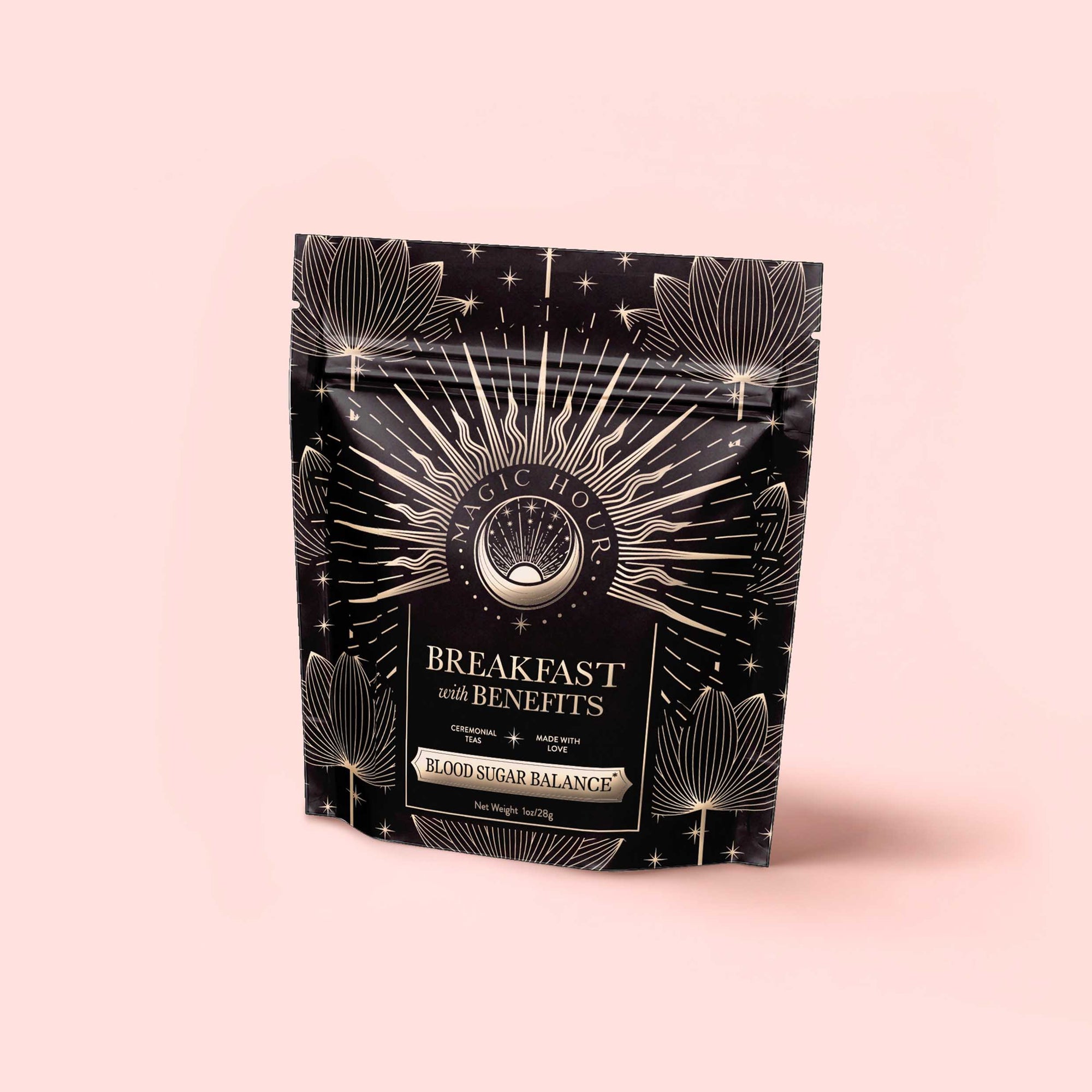 A black and gold resealable pouch labeled "Blood Sugar Balance: Breakfast with Benefits," adorned with starburst and floral designs, stands upright on a pale pink background—an herbal tea blend featuring Assam black tea and Gymnema Sylvestre.