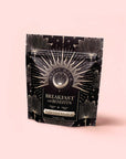 A black and gold resealable pouch labeled "Blood Sugar Balance: Breakfast with Benefits," adorned with starburst and floral designs, stands upright on a pale pink background—an herbal tea blend featuring Assam black tea and Gymnema Sylvestre.