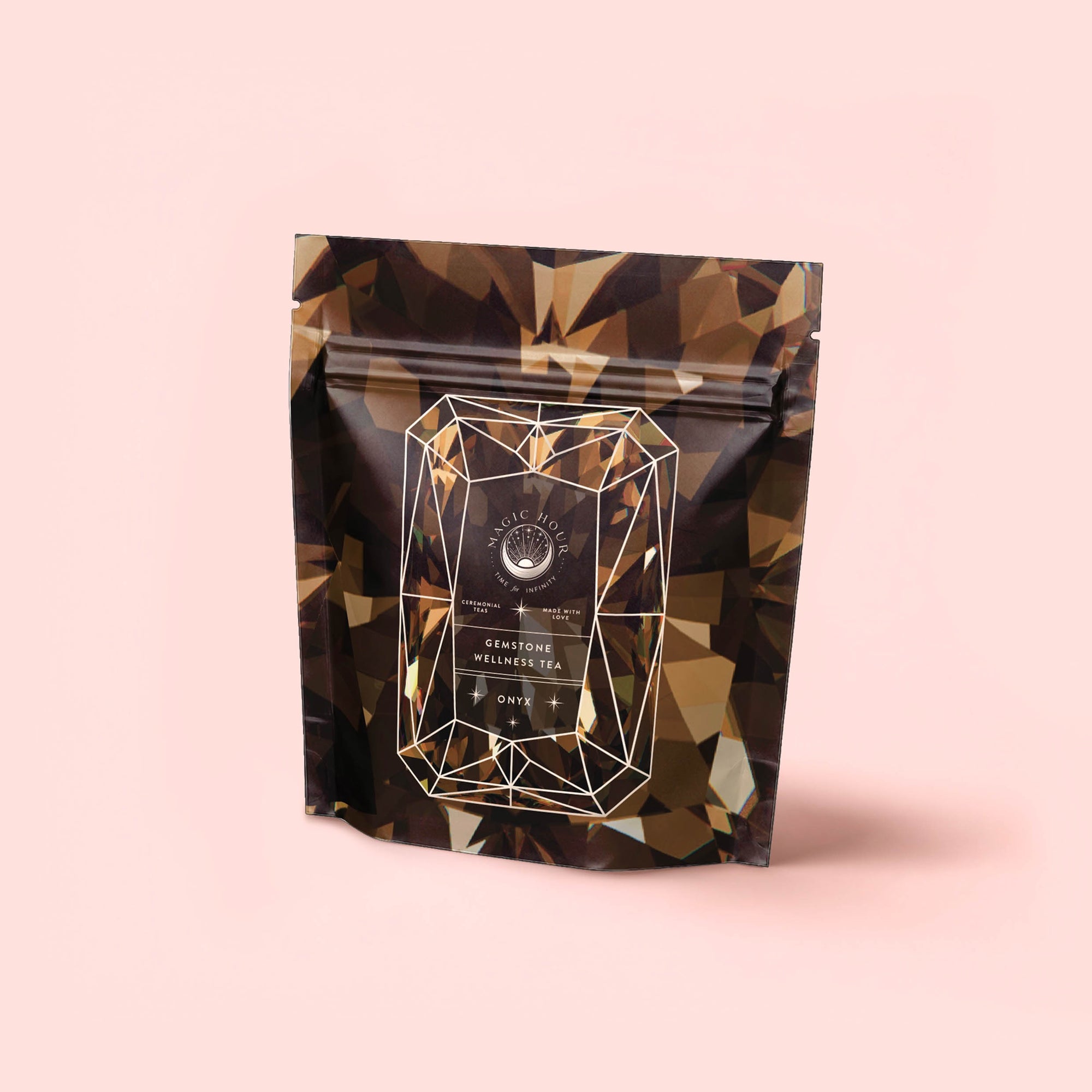 A resealable pouch with a geometric gemstone design and dark brown tones, labeled "Black Onyx - Chaga Maca Toffee Elixir for Energy, Immunity & Good Fortune," features a caffeine-free blend against a pale pink background.