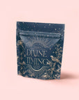 A dark blue pouch labeled "Divine Timing Balance" features gold celestial and floral illustrations, stars, and birds. Designed for women's wellbeing and menopause support, the packaging is set against a soft pink background.