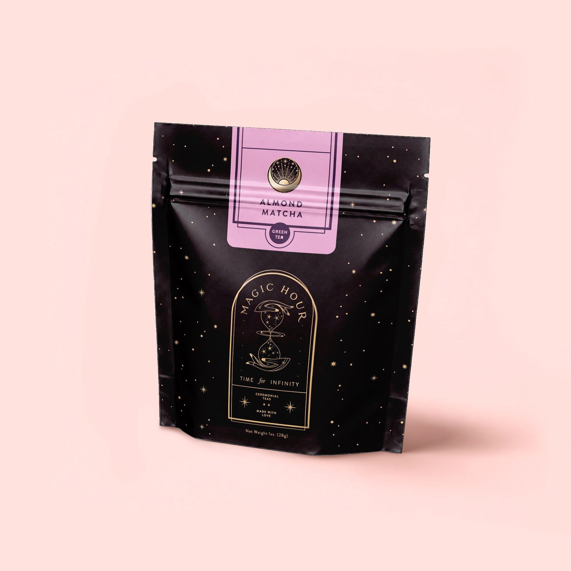 A black resealable pouch with gold star patterns labeled "Magic Hour" and "Time + Infinity," featuring a purple label that reads "Antioxidant-rich Almond Matcha Green Tea for Joy." The bag is set against a pale pink background.