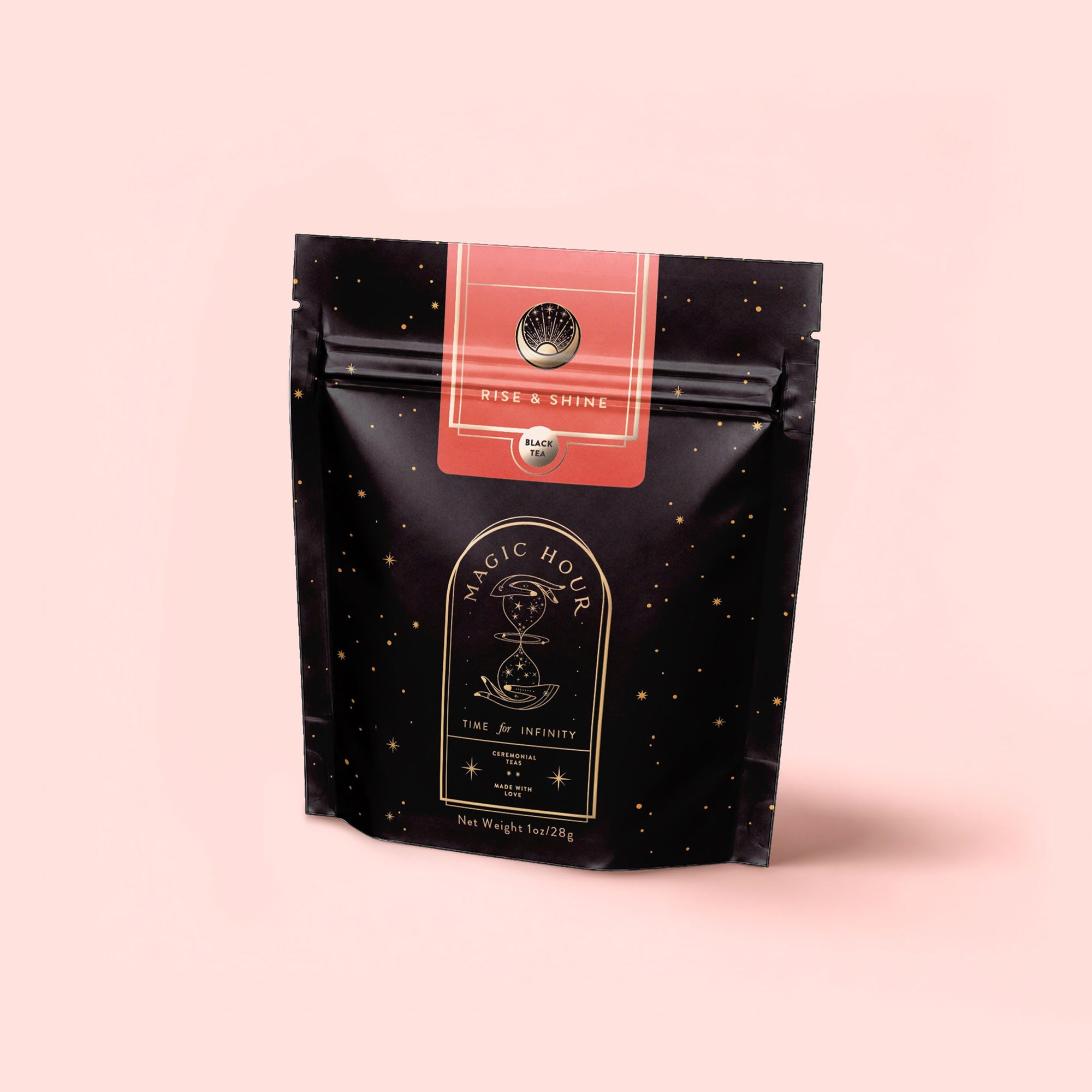 A black resealable pouch labeled "Magic Hour" with gold stars and a celestial design contains Rise & Shine Black Tea, an adaptogenic wellness blend. The pouch features a pink label and stands against a pale pink background.