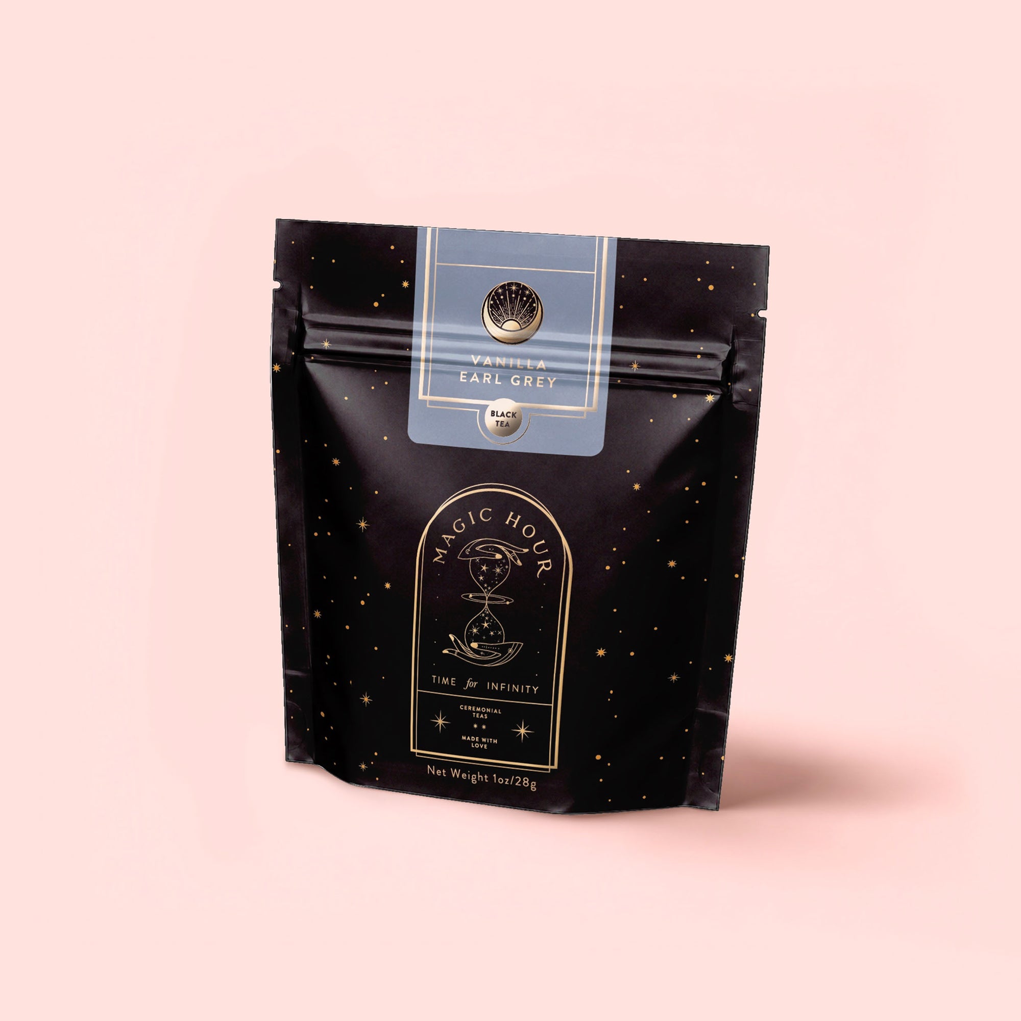 A black pouch labeled "Vanilla Earl Grey: Tea for the Lushness of Life" stands upright against a soft pink background, featuring gold and white text with celestial-themed graphics.