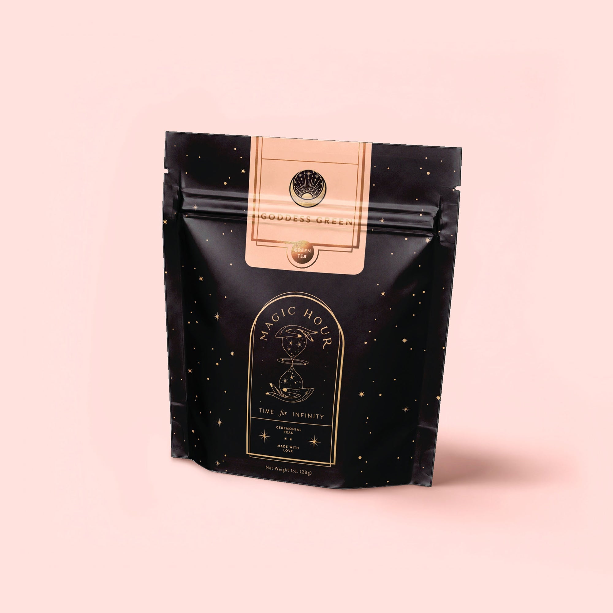 A black and gold resealable pouch labeled "Magic Hour" with celestial designs and "Goddess Green Tea" text sits on a pale pink background. The mystical packaging hints at flavors of apricot lychee and organic lemongrass.