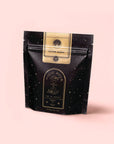 A black, star-speckled pouch labeled "Magic Hour" with a gold accent and "Silver Moon White Tea: Yin Zhen Silver Needle" stands upright against a pale pink background.