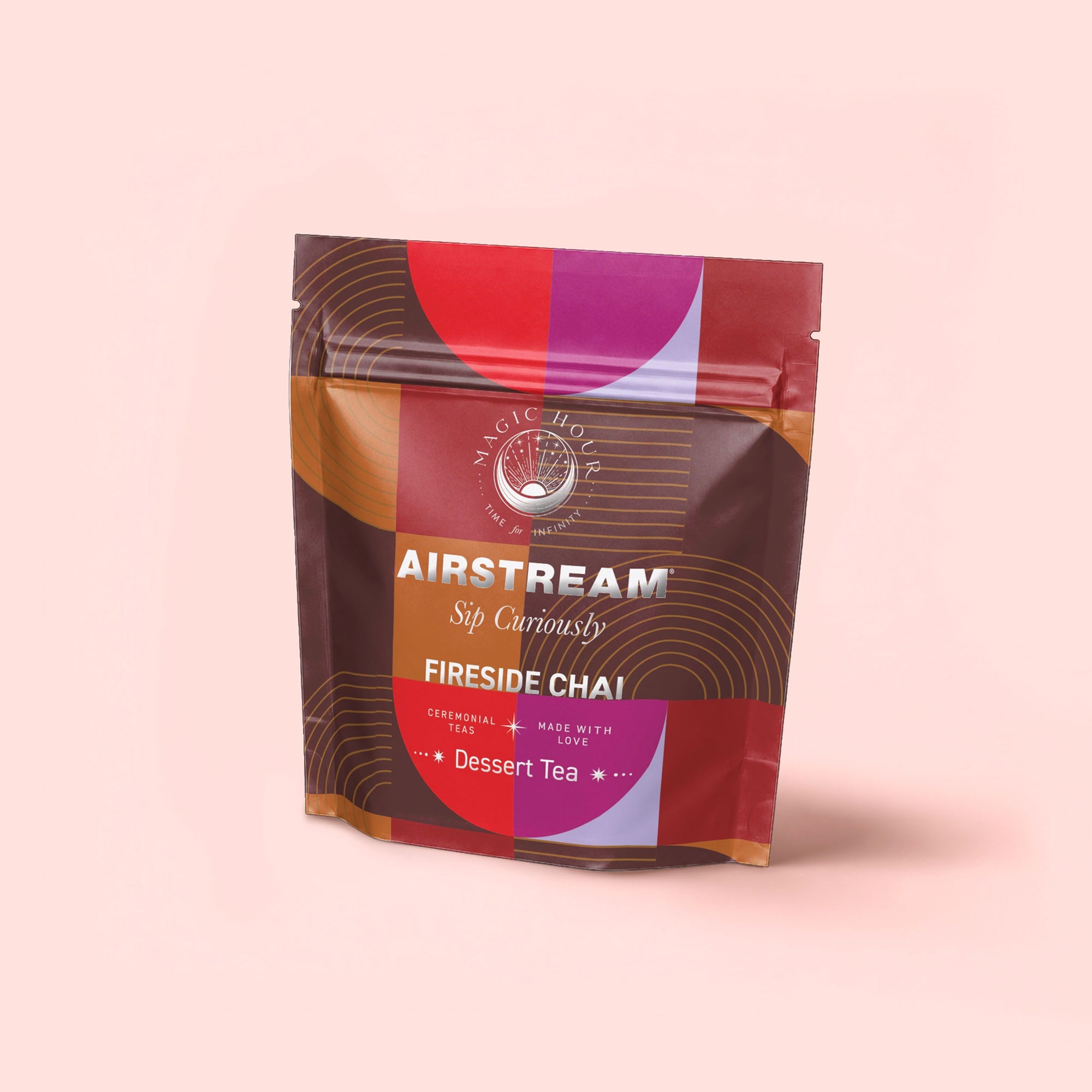 A colorful resealable pouch labeled "Airstream Sip Curiously, Pumpkin Spice Fireside Chai, Dessert Tea" with geometric designs stands against a pale pink background, showcasing this antioxidant-rich, caffeine-free tea.