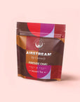 A colorful resealable pouch labeled "Airstream Sip Curiously, Pumpkin Spice Fireside Chai, Dessert Tea" with geometric designs stands against a pale pink background, showcasing this antioxidant-rich, caffeine-free tea.