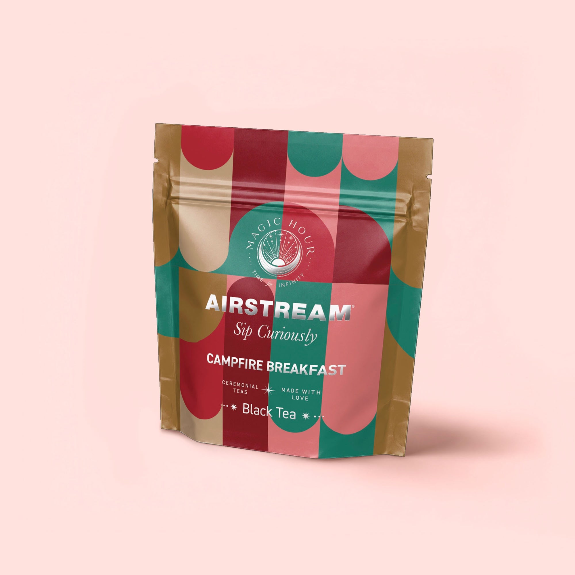 A vibrant pouch of Campfire Breakfast: Golden Tipped Assam, Puerh & Lapsang Souchong Pine Smoked Connoisseur's Cup for Nostalgic Mornings stands upright on a light pink background—an ideal smoky tea or coffee alternative.