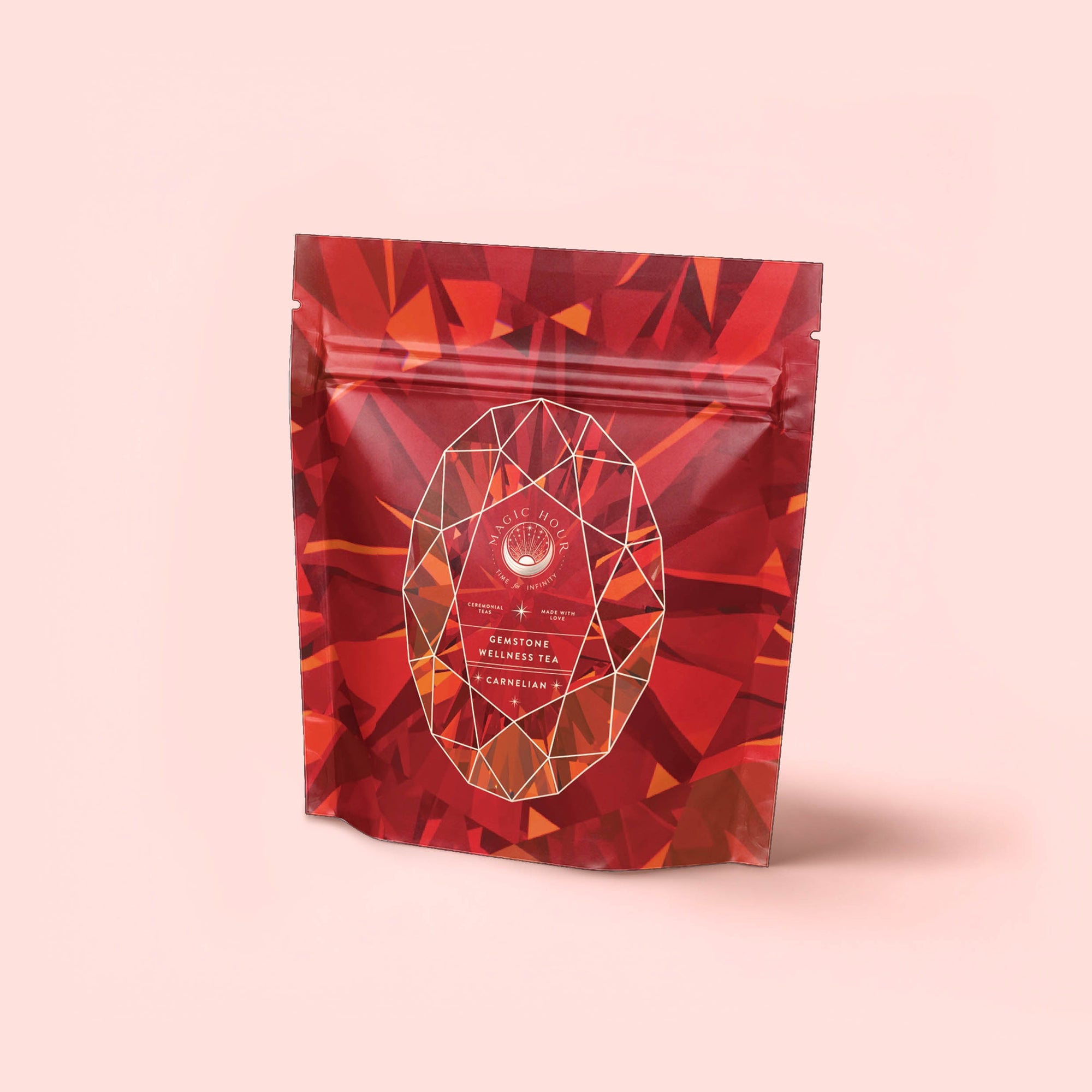 A red and orange resealable pouch with geometric patterns, featuring an oval label that reads “Carnelian: Caffeine-Free Apricot Amaretto Tea” on a light pink background.