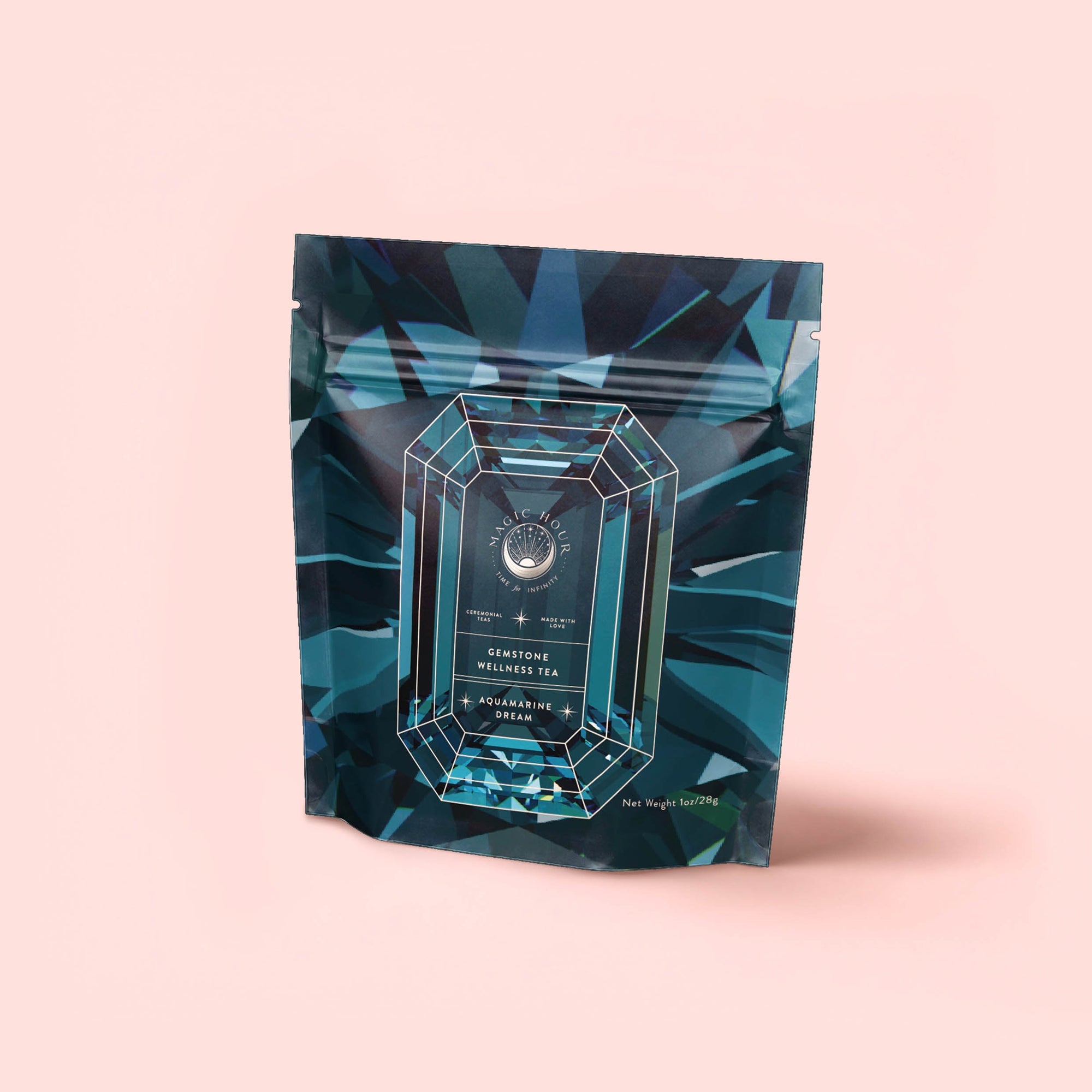 A teal and blue geometric tea package with a gemstone design stands upright on a light pink background. The label reads “Aquamarine Dream – Soothing Herbal Ayurvedic Adrenal Tonic.” Net weight and logo are visible.
