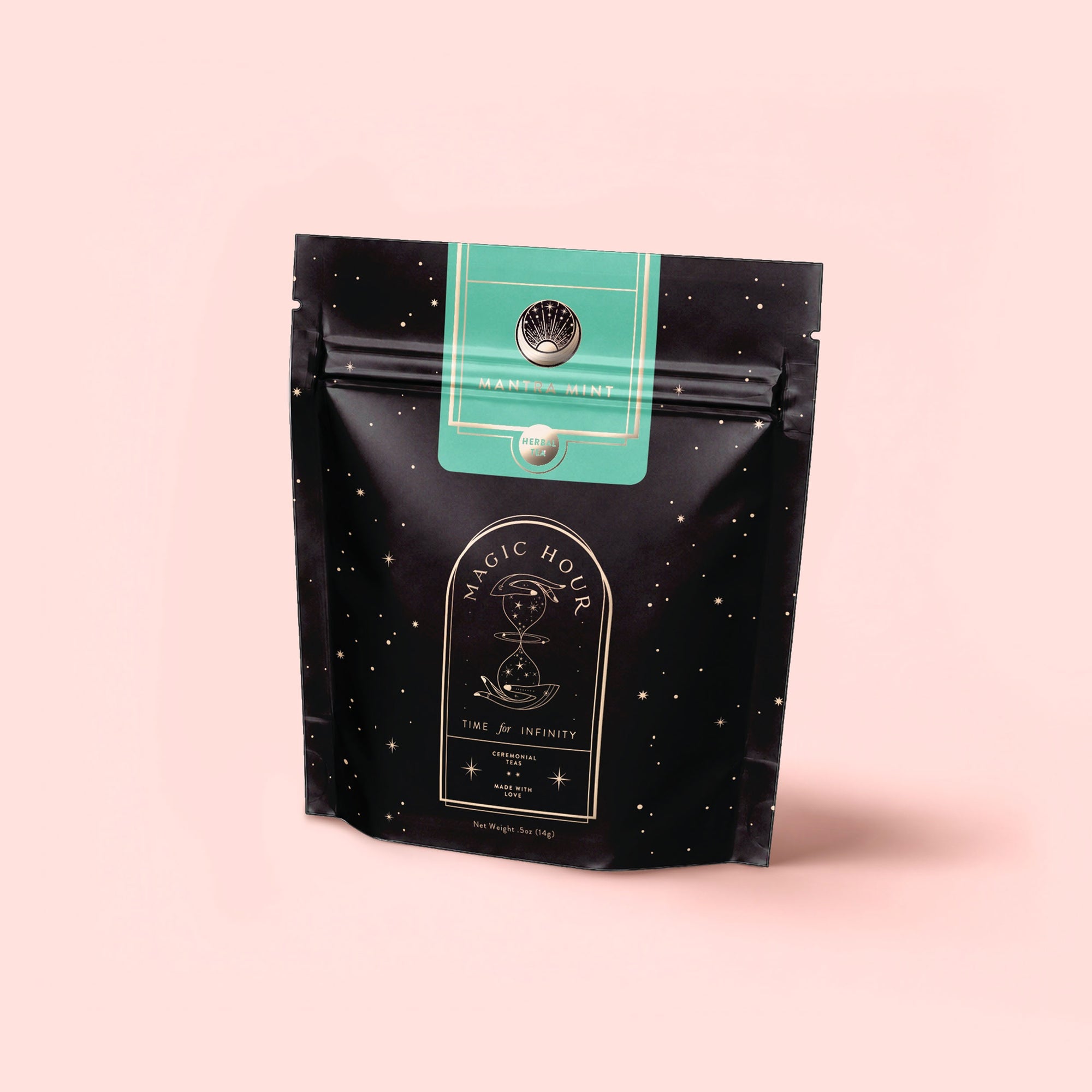 A standing black resealable pouch labeled "Magic Hour" with a celestial design and green top label showcases Mantra Mint™ Herbal Tea, featuring calming Ashwagandha. Set against a pale pink background, this blend is naturally caffeine-free.
