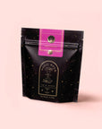 A black resealable pouch with gold star patterns and a pink label at the top features Magic Hour's "Soulmate: Chocolate-Raspberry-Rose Black Tea for Finding & Celebrating Love" against a light pink background.