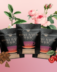 Three black pouches of “Small Batch Magic Valentine’s 2026” are displayed before illustrated pink roses, chocolate pieces, cherries, and green leaves on a pink gradient. The teacup packaging highlights chocolate cake tea and white tea flavors.
