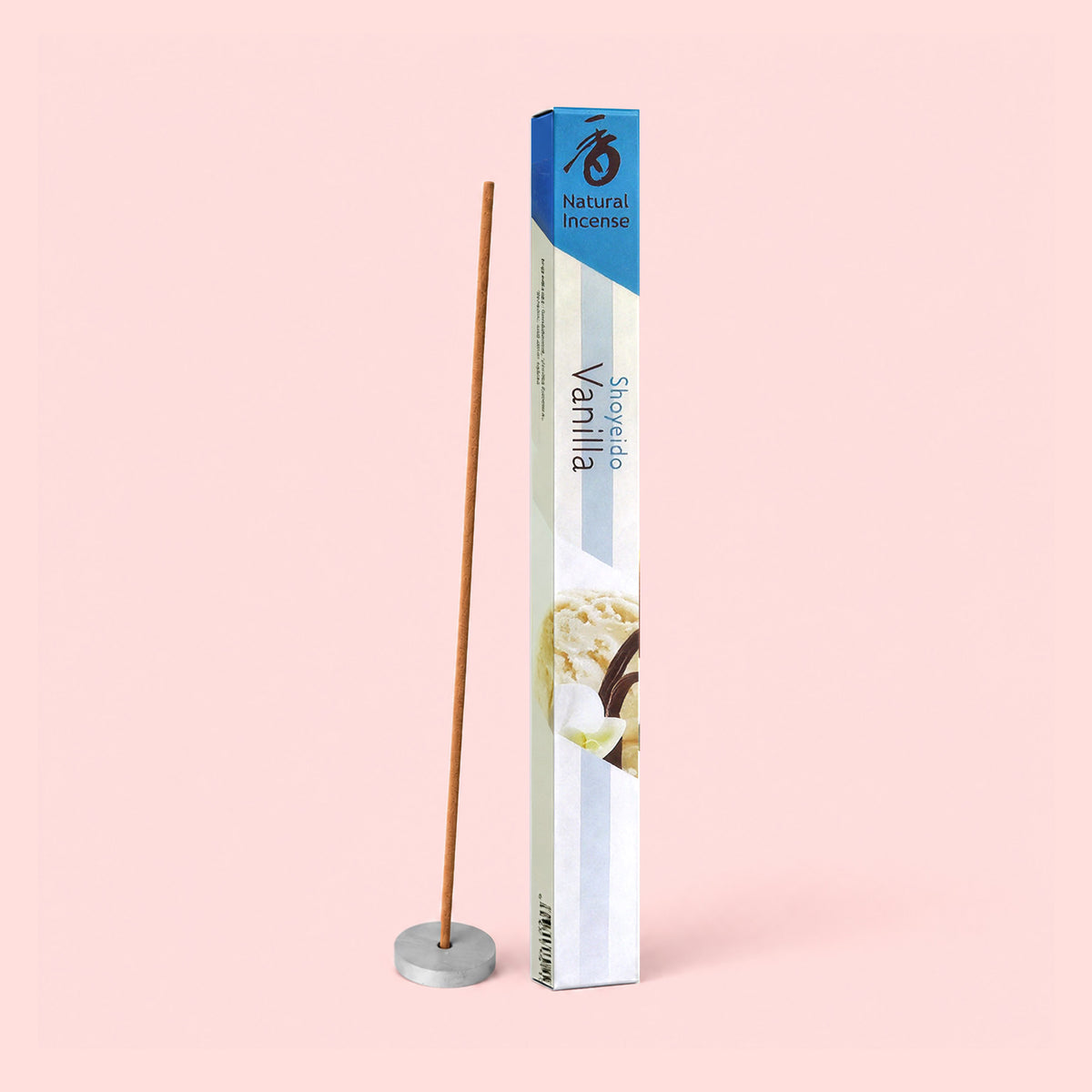 A Natural Incenses : Vanilla stick, infused with the rich aroma of Madagascar vanilla, stands in a round holder beside a tall, rectangular blue and white box marked “Natural Incenses : Vanilla,” all set against a light pink background.