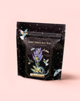 A black resealable bag labeled "Vanilla Lavender Black Iced Tea" features whimsical lavender, butterflies, and gold celestial designs, highlighting its blend of organic Assam black tea and lavender essential oil.