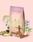 A pastel tea package labeled "Vata: Caffeine-Free Saffron-Rose Spice Tea" sits with cinnamon sticks, saffron flowers, fennel, and herbs—a perfect caffeine-free adaptogenic blend for your Ayurvedic evening ritual.