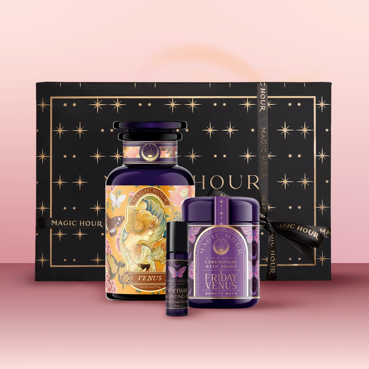 The Venus Bath & Beauty Box is a luxury self-care gift set with a decorative bottle, jar, and small tube adorned in purple and gold, beautifully arranged before a black and gold star-patterned box on a pink backdrop.