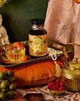 A vibrant display with a golden teapot, glass teacup of Venus - Tea for Beauty Sleep, colorful tea container, fresh grapes and raspberries, small statue, all set against floral pattern fabric.