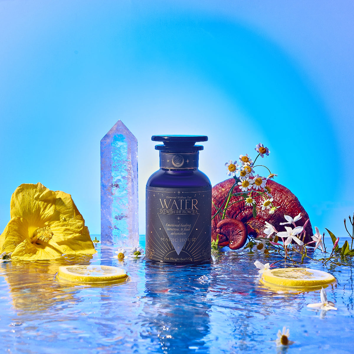 A dark blue Water bottle rests on a reflective watery surface, surrounded by yellow flowers, sliced citrus, white daisies, a crystal, and a halved plum, set against a vivid blue backdrop.
