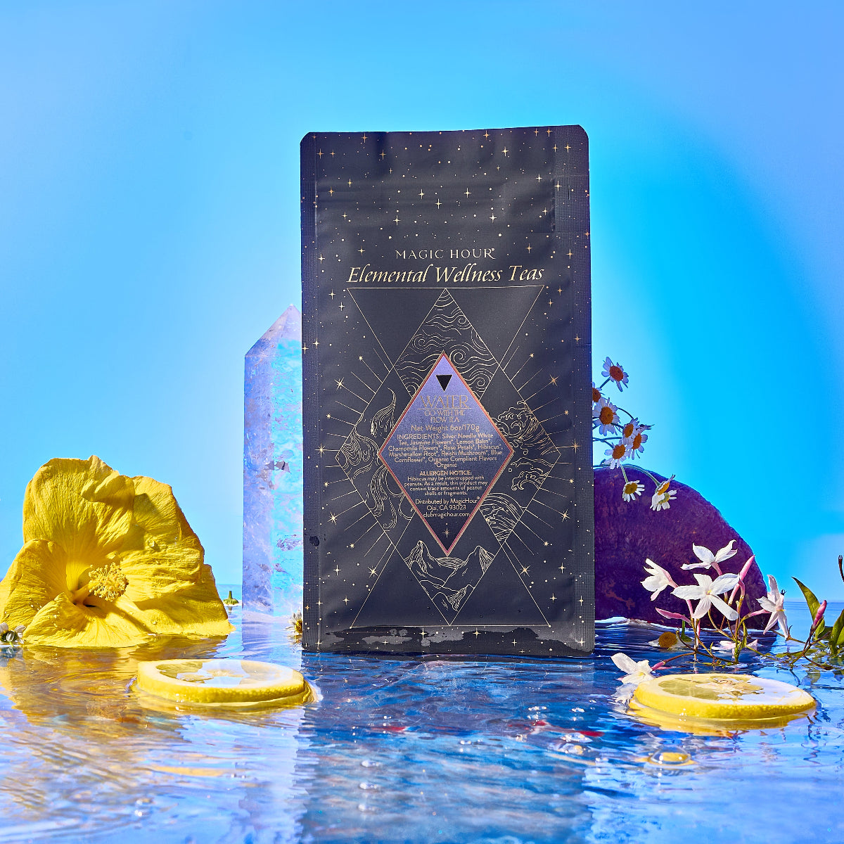A bottle of Water stands on rippling water, surrounded by yellow and white flowers, lemon slices, and crystals, against a vibrant blue background.