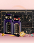 The Wake Up & Wind Down Tea Gift Set features two dark purple "Magic Hour" bottles, a tea ceremony towel, gold tea infuser, golden wand stirrer, and a wrapped crystal arranged before a starry black box—a true tea ritual experience.
