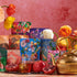 A colorful display showcasing the vibrant Wanderlust Sampler Tea Set, featuring floral and botanical designs, arranged against a pink wall. The scene includes blooming flowers, fresh pomegranates, a glass honey pot with a honey dipper, and a golden teapot.