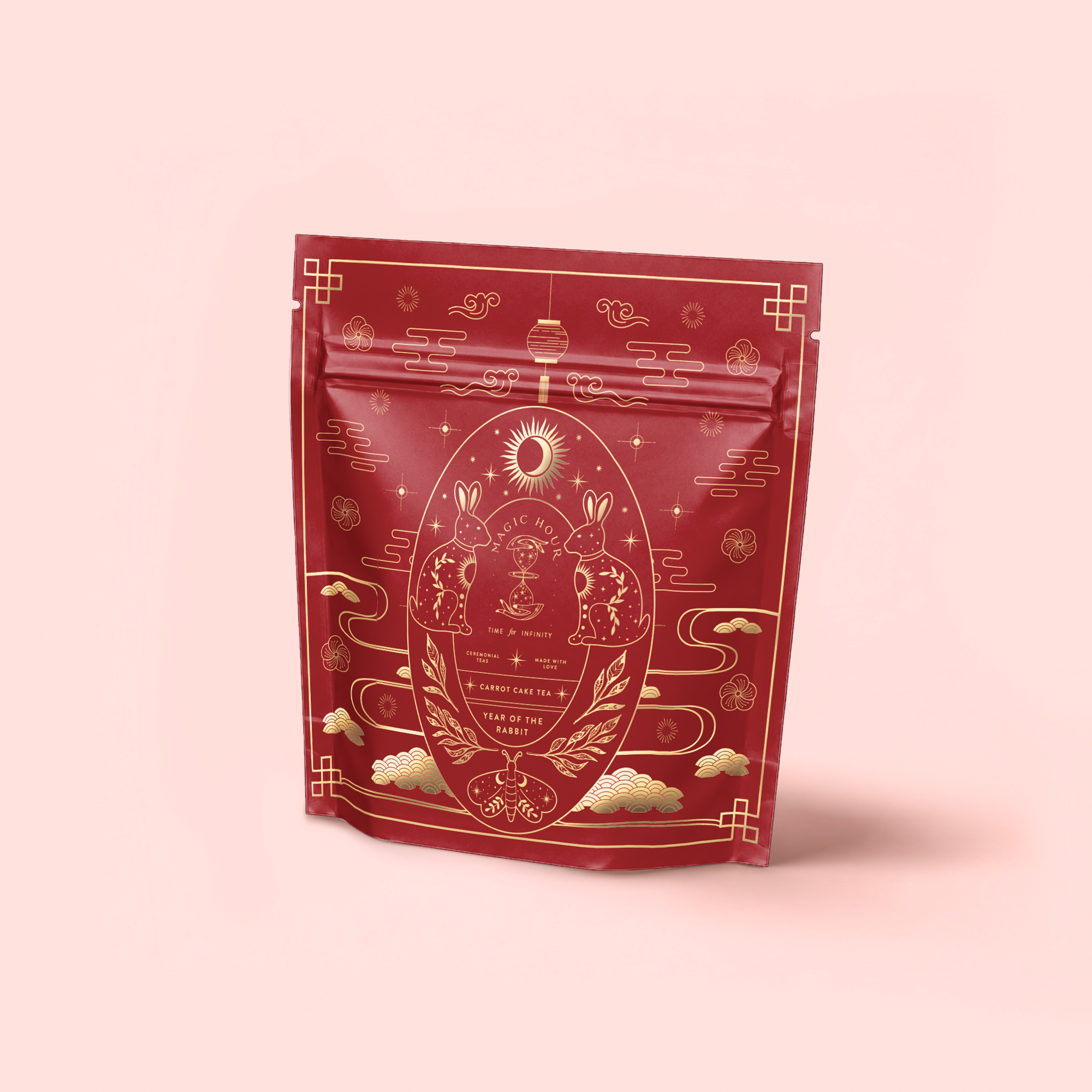The Year of the Rabbit Carrot Cake Tea comes in a red, resealable pouch featuring gold rabbit, cloud, and celestial designs on light pink—an elegant East Asian-inspired look ideal for Chinese New Year or caffeine-free tea enthusiasts.