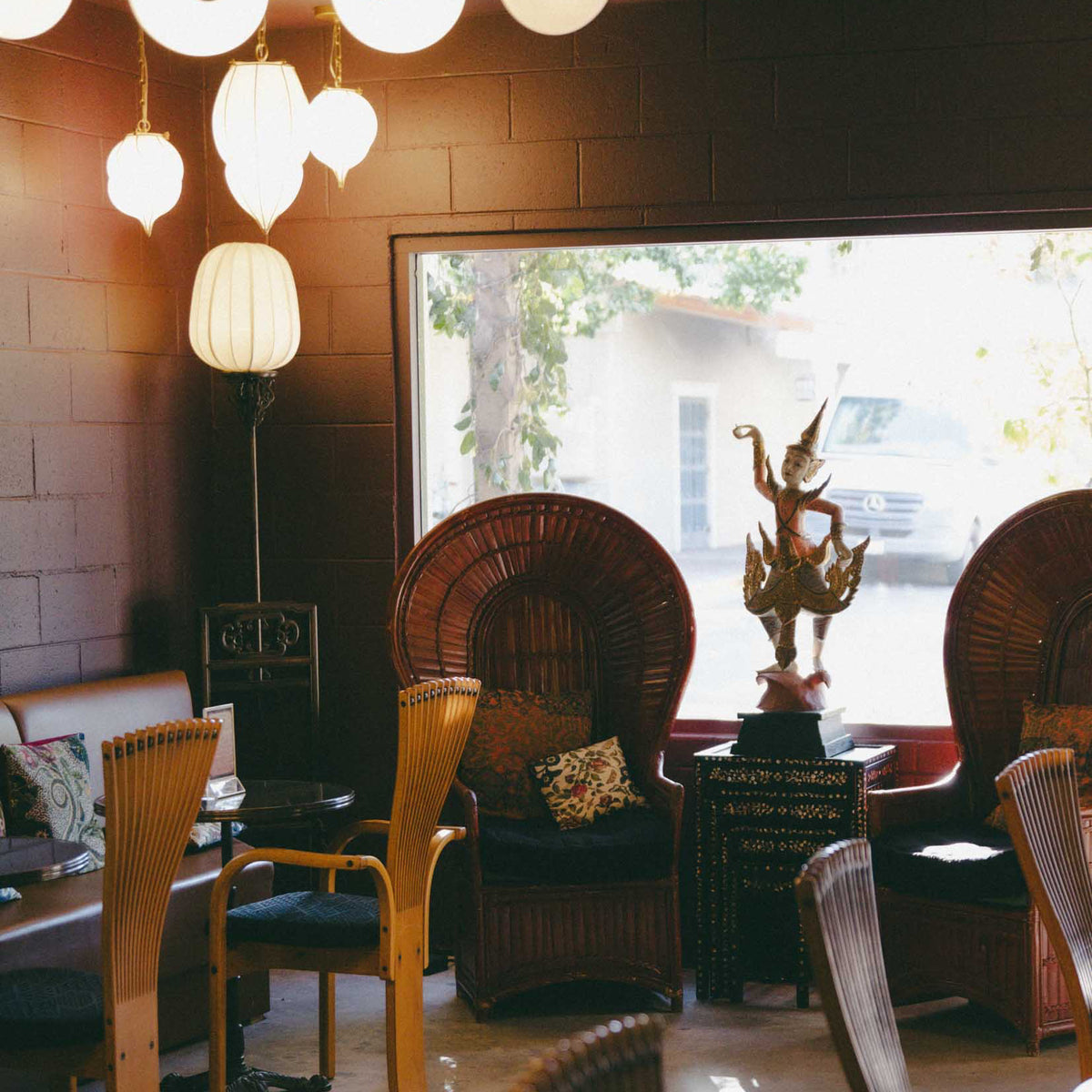 A lounge area at The Soul of Tea: A Two Day Retreat in Ojai, CA featuring wicker peacock chairs and a carved Thai-style figure standing on a side table.