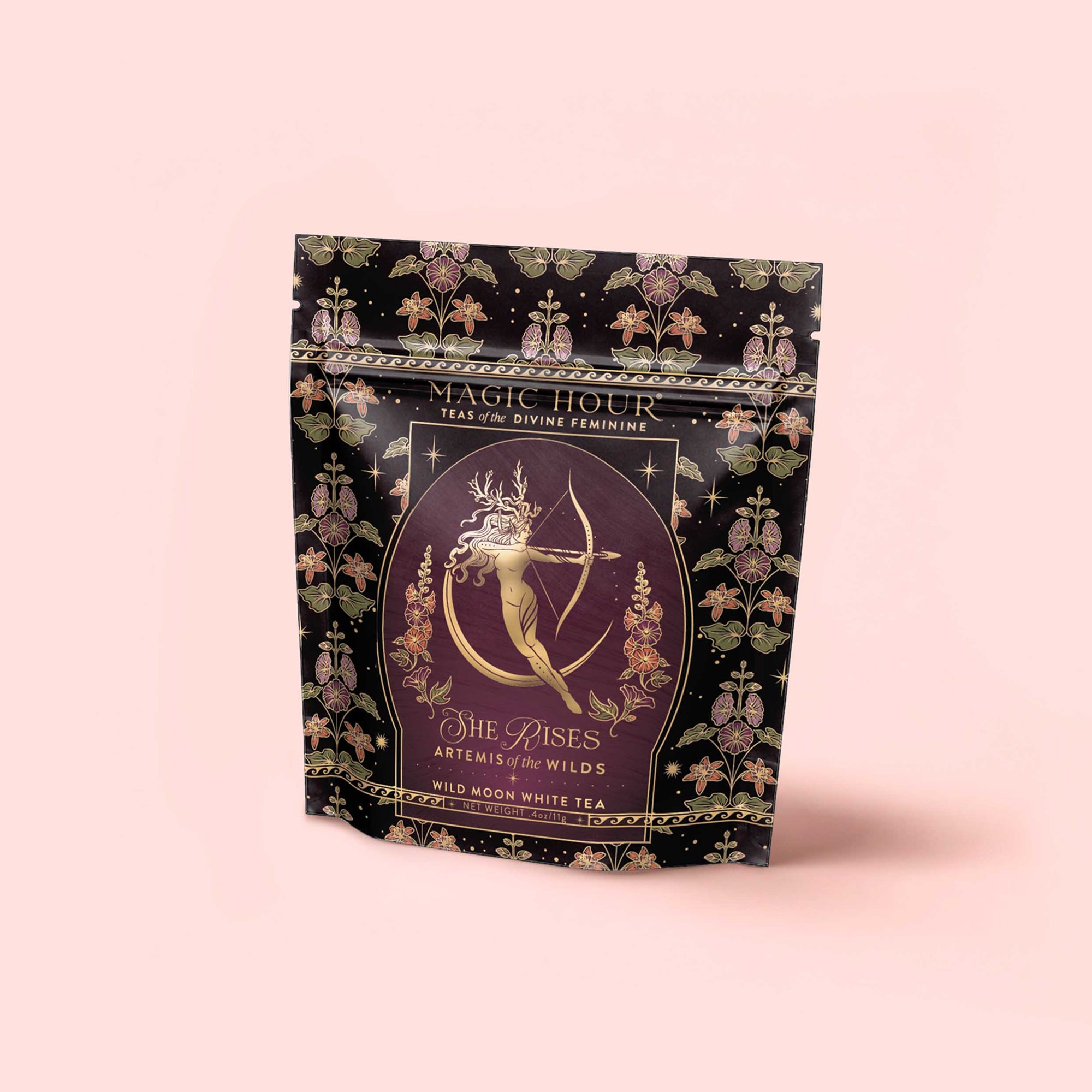 A decorative pouch from the Monthly Magic Tea Journey Subscription features "She Rises" Wild Moon White Tea, inspired by goddess ritual, with Artemis drawing a bow amid ornate floral patterns on a pink background.