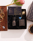 A neatly arranged flat lay showcases a "Gemini Astrology Tea Gift Set," featuring a tea box, a tea infuser, and a cup of luxury tea on a wooden tray with dried tea leaves and moon-shaped accessories. Soothing botanicals enhance the scene, while a blooming protea flower adds a natural touch against the light background.