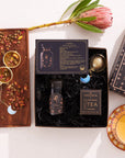 The Libra Astrology Tea Gift Set embraces a tea-themed design and features a "Libra" card, a canister of Moonlight White Tea, a gold infuser, and a floral display. Its box is adorned with starry patterns, complemented by herbs and flowers arranged on a wooden tray for an enchanting presentation.