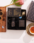 Flat lay of the Virgo Astrology Tea Gift Set, showcasing a decorative box labeled "Magic." The set includes a jar of loose tea made with organic ingredients, a card labeled "Virgo," a tea infuser, and a wooden tray adorned with moon-shaped charms. Enhance your ritual by enjoying this wellness blend and sip of tea.