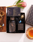 The Sagittarius Astrology Tea Gift Set is a decorative box featuring themed tea items such as a jar and an Opalite Moon Tea Strainer. Accompanied by a cup of tea on a wooden tray with dried herbs and a flower, the celestial packaging elevates this astrology tea experience.